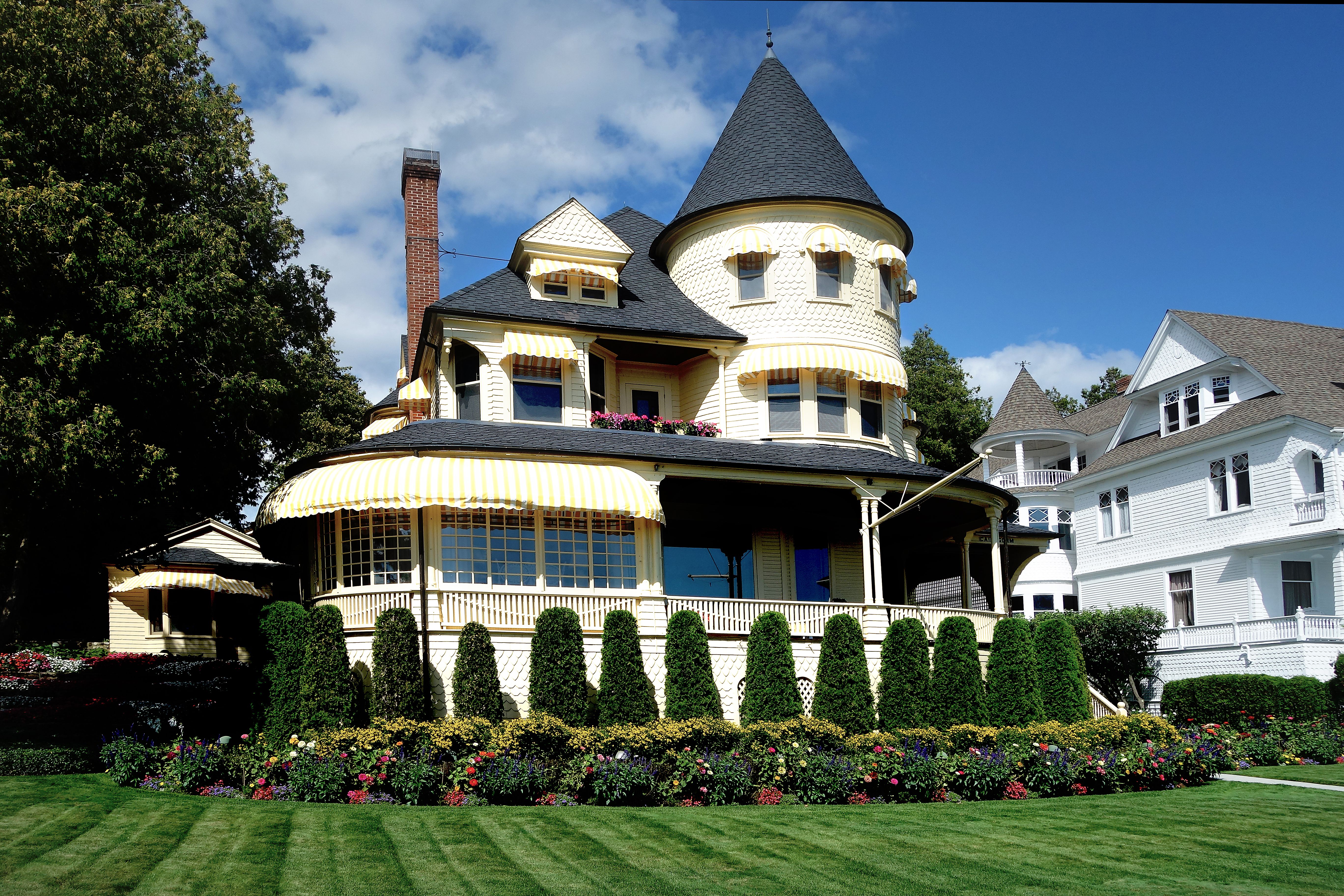 Victorian house with a wraparound porch, turret, and white siding, set behind a landscaped garden.