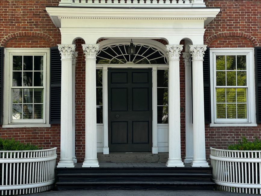 Colonial style house entrance with white columns and black shutters. Traditional architectural design.