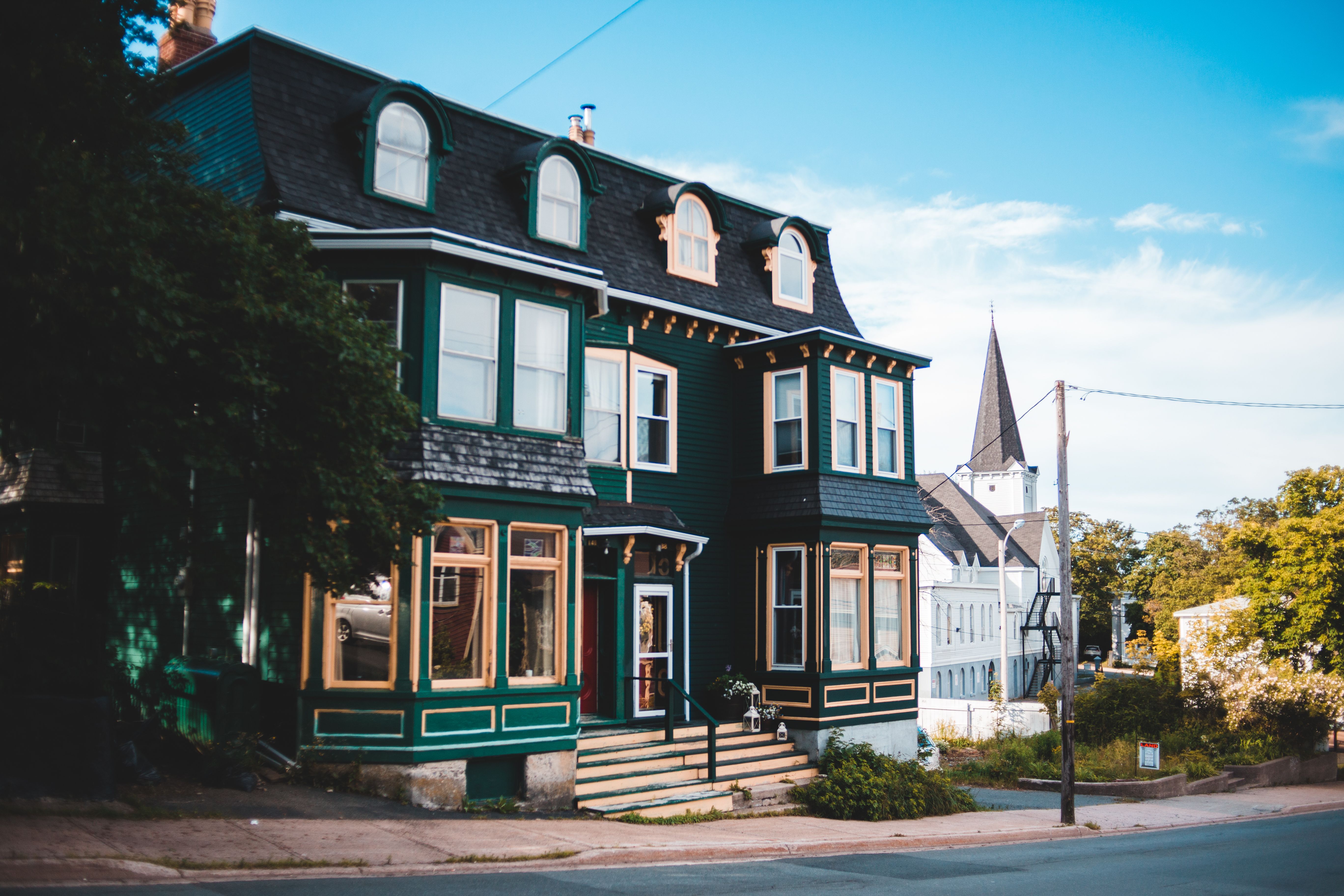 Freshly painted dark green Victorian house with cream trim on a small-town street.
