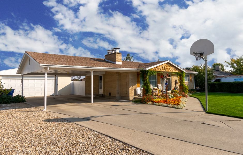 Charming suburban home with a basketball hoop, garage, and vibrant garden under a clear sky.